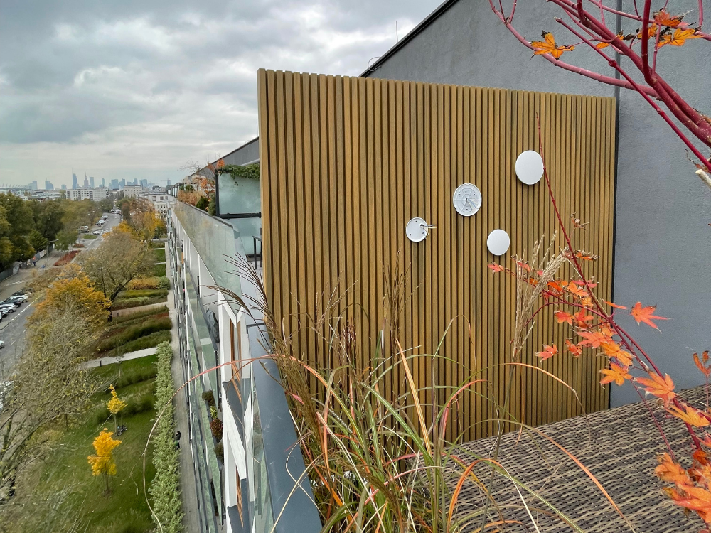 Lamele elewacyjne kompozytowe UltraShield® Naturale w kolorze Oak w roli przepierzenia pomiędzy balkonami w bloku mieszkalnym