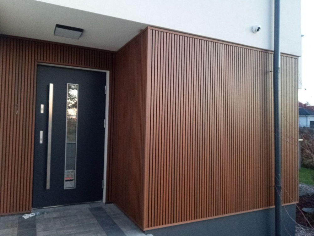 Lamele kompozytowe na elewację UltraShield® Naturale UH46 w kolorz Teak zamontowane przy drzwiach i na ścianie narożnej domu jednorodzinnego