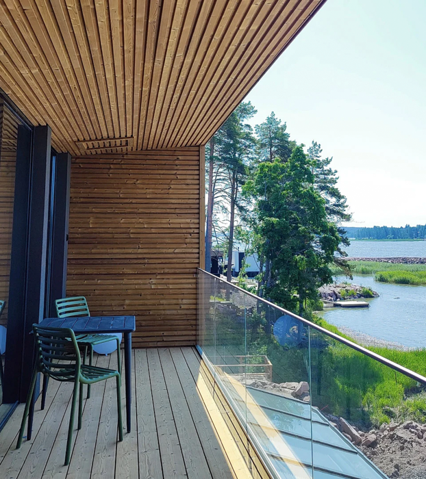 Nowoczesny balkon z drewnianym wykończeniem i szklaną balustradą, z widokiem na jezioro i otaczającą zieleń