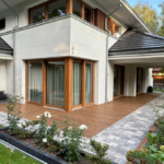 Biały dom w oddali i taras z drewnianych desek kompozytowych.