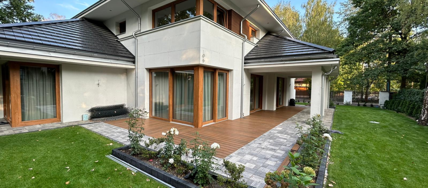 Biały dom w oddali i taras z drewnianych desek kompozytowych.