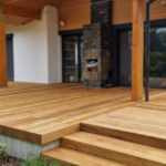 Drewniany taras z zadaszeniem i kamiennym grillem przy domu jednorodzinnym.