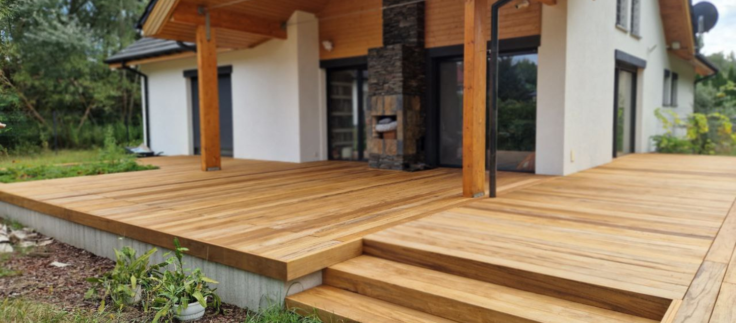 Drewniany taras z zadaszeniem i kamiennym grillem przy domu jednorodzinnym.